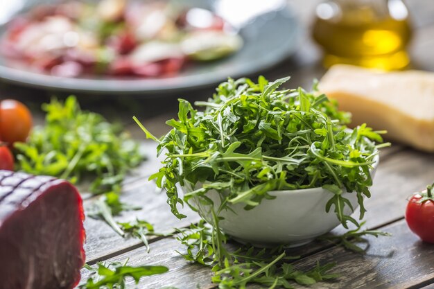 Fresh arugula salad in white dish on wooden table.