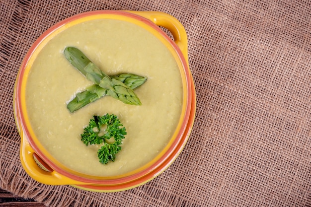 Fresh asparagus creamy soup and ingredients on wooden table, selective focus