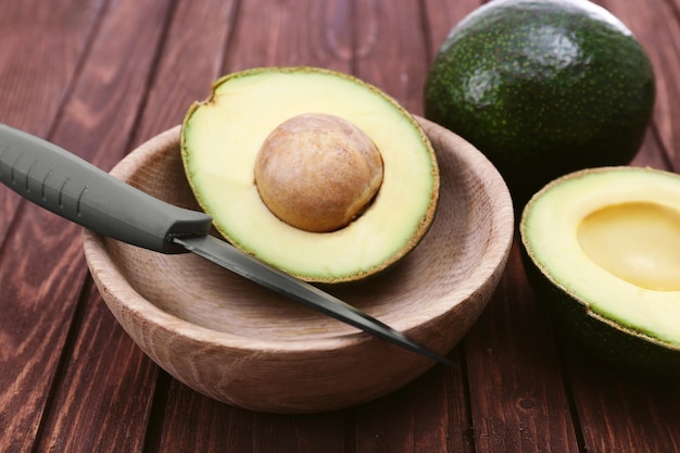 Fresh avocado in bowl on wooden background