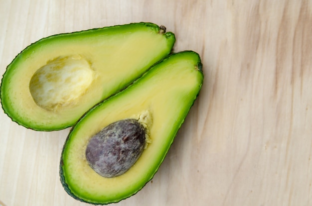 Fresh avocado fruit cut in half on white wooden board