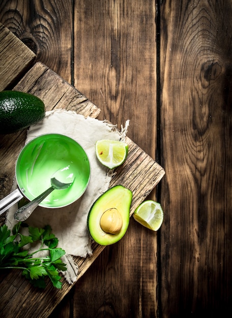 Fresh avocado sauce, lime and herbs. On wooden background.