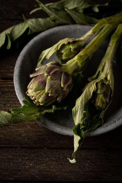 Fresh baby artichoke with leaves on rustic wooden background