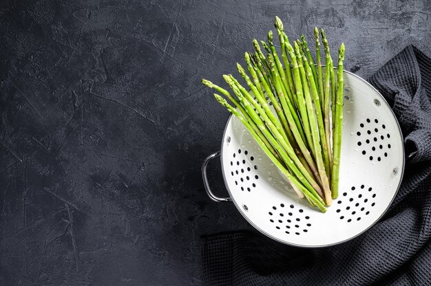 Fresh baby green asparagus in a colander. Black background