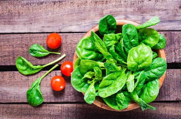 Gli spinaci freschi del bambino lasciano in una ciotola e nei pomodori ciliegia su una tavola di legno