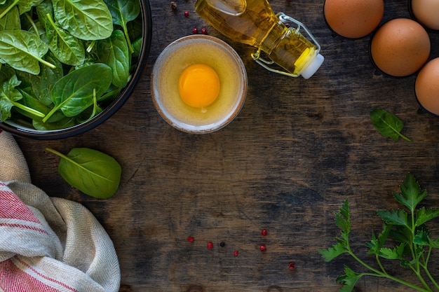 Fresh baby spinach leaves in a bowl and eggs on a wooden table. Top view. Copy space