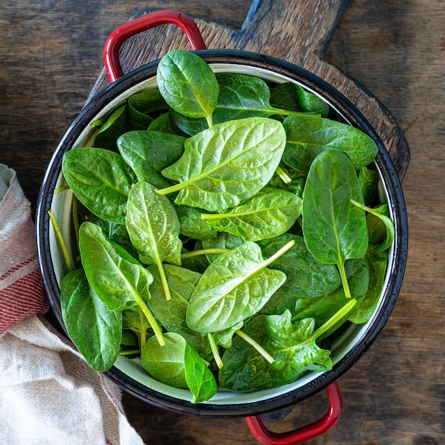 Fresh baby spinach leaves in a bowl on a rustic wooden table. Square