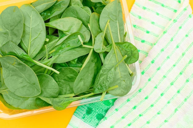 Fresh baby spinach leaves in transparent plastic package on yellow background