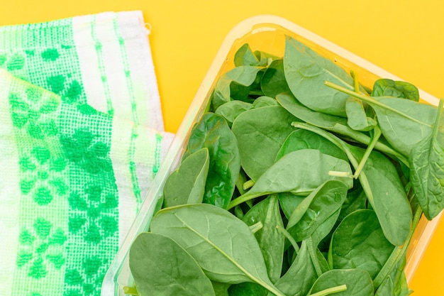 Fresh baby spinach leaves in transparent plastic package on yellow background