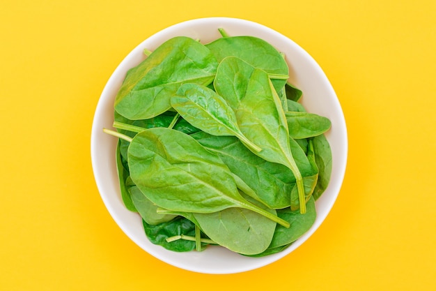 Fresh baby spinach leaves in white bowl on yellow background