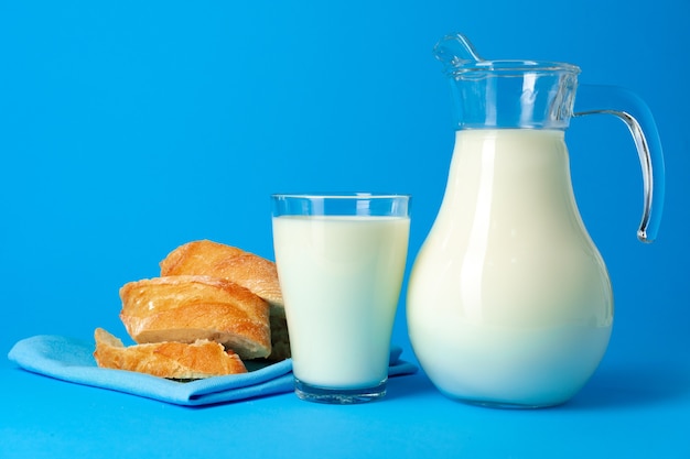 Fresh baguette bread and pitcher with fresh milk on blue close up
