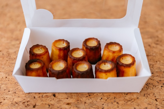 Fresh baked Canelés inside white paper box. 