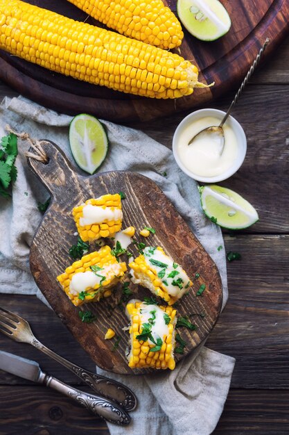 Fresh baked corn cobs with aioli sauce and cilantro on rustic wooden background