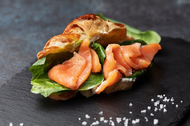 Foto panino croissant appena sfornato con insalata e salmone su una tavola di ardesia nera