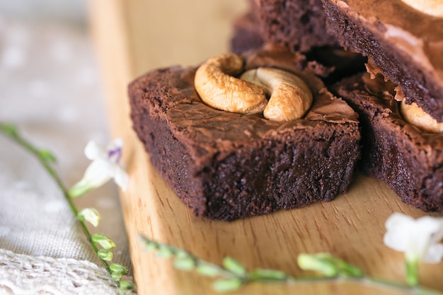 Фото Свежие испеченные пирожные помадки темного шоколада покрывая с орехом кешью штабелированным на деревянной плите. вкус вкусный, горьковато-сладкий, жевательный и нежный. брауни - один из видов шоколадного торта. концепция домашней выпечки.