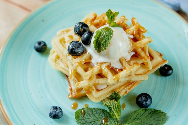 Le cialde belghe casalinghe classiche al forno fresche hanno completato con gelato, i mirtilli freschi e la menta su fondo di legno, vista dall'alto in basso. concetto di colazione