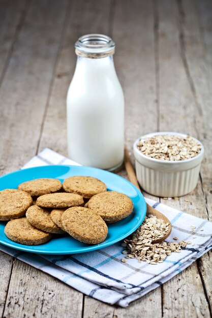 Fresh baked oat cookies on blue ceramic plate on linen napkin, bottle of milk and oak flakes 