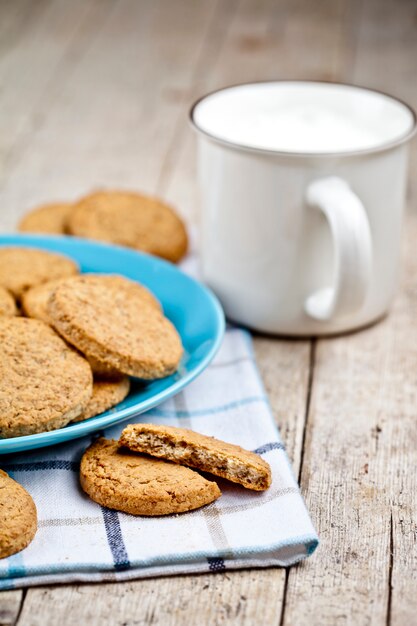 Fresh baked oat cookies on blue ceramic plate on linen napkin and cup of milk.