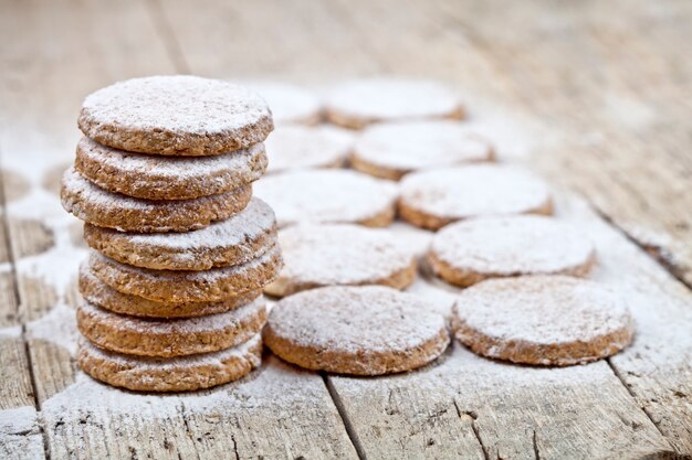 Fresh baked oat cookies with sugar powder on rustic wooden table.