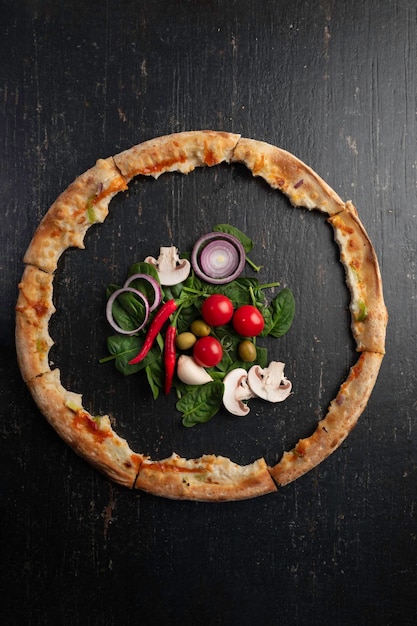 Foto pizza al forno fresca con ingredienti su un tavolo di pietra scuro