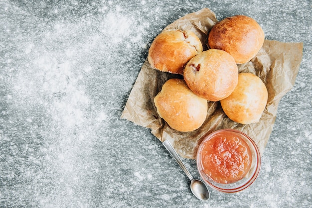 Fresh baked yeast buns filled with apple jam on gray background with flour.