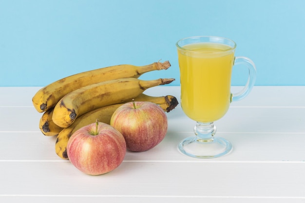 Fresh bananas apples with a glass of juice on a white table