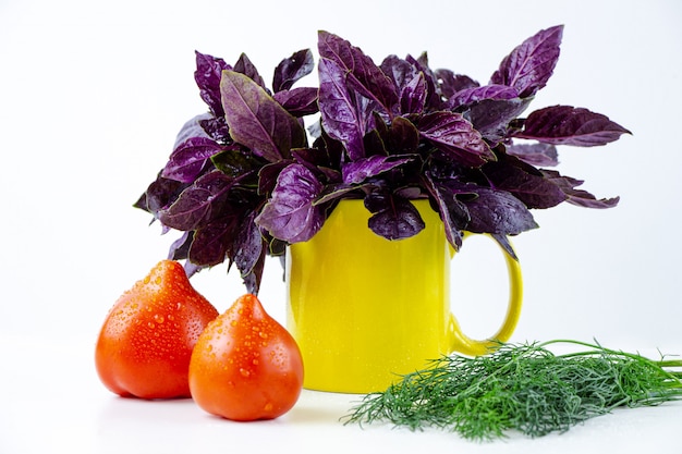 Sul tavolo si trovano basilico fresco, aneto e due pomodori rossi.