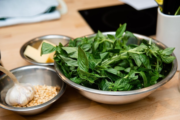 Fresh basil leaves garlic and pine nuts parmesan cheese in metal bowls on wooden table