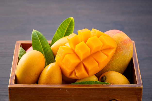 Свежие и красивые плоды манго в деревянной коробке с нарезанными кубиками кусками манго на темном деревянном фоне, пространство для копирования (пространство для текста), пробел для текста