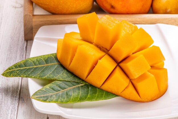 Fresh and beautiful mango in a white plate with sliced diced mango chunks isolated with light wooden background, copy space(text space), blank for text