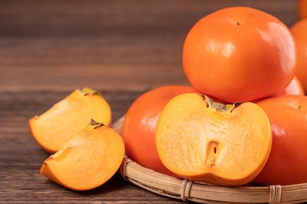 Fresh beautiful orange color persimmon kaki on bamboo sieve over dark wooden table Seasonal traditional fruit of Chinese lunar new year close up