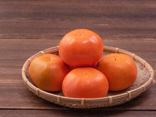 Fresh, beautiful orange color persimmon kaki on bamboo sieve over dark wooden table.