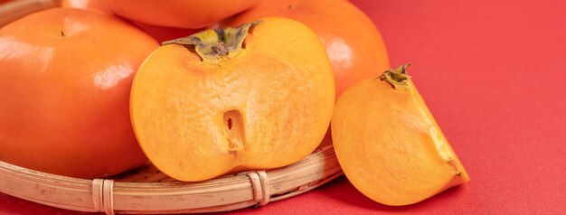 Fresh beautiful sliced sweet persimmon kaki isolated on red table background and bamboo sieve Chinese lunar new year design concept close up