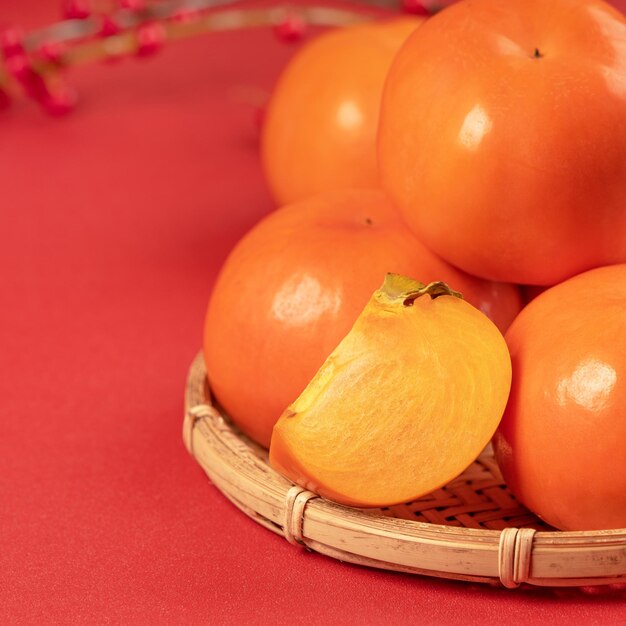 Fresh beautiful sliced sweet persimmon kaki isolated on red table background and bamboo sieve Chinese lunar new year design concept close up