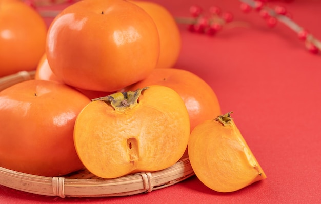 Fresh beautiful sliced sweet persimmon kaki isolated on red table background and bamboo sieve Chinese lunar new year design concept close up