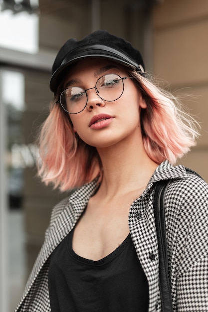 Photo fresh beautiful young woman with stylish glasses and a vintage hat in a fashion plaid shirt is walking in the city