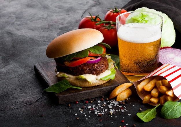 Hamburger di manzo fresco con salsa e verdure e bicchiere di birra artigianale chiara con patatine fritte sulla cucina di pietra.