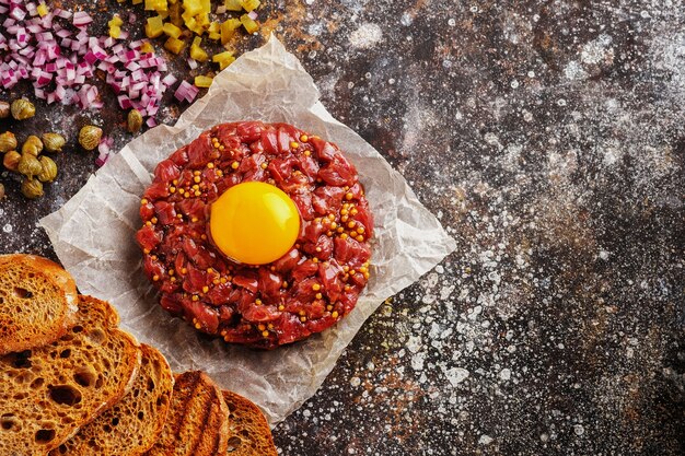 Fresh beef tartare with yolk, capers, onions and mustard, top view. Flat lay.