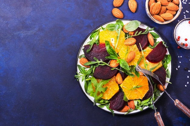 Fresh Beetroot Salad with Orange arugula and almonds nut on blue background Vegan healthy summer food Flat lay Copy space