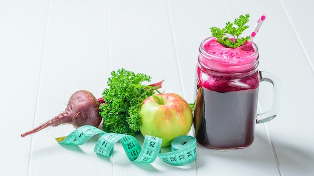 Fresh beetroot smoothie, apple, parsley and measuring tape on white wooden table.