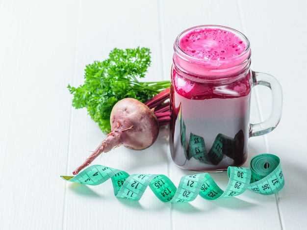 Fresh beetroot smoothie, measuting tape and parsley on white wooden table