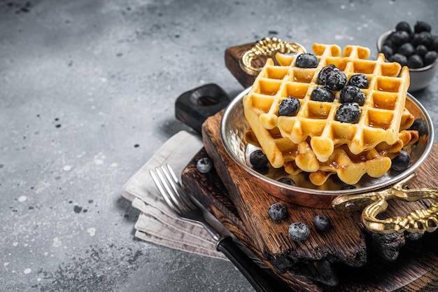 Fresh Belgian waffles with blueberry and Syrup in skillet. Gray background. Top view. Copy space.