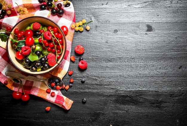 Fresh berries in a cup on the old fabric. On a black wooden table.