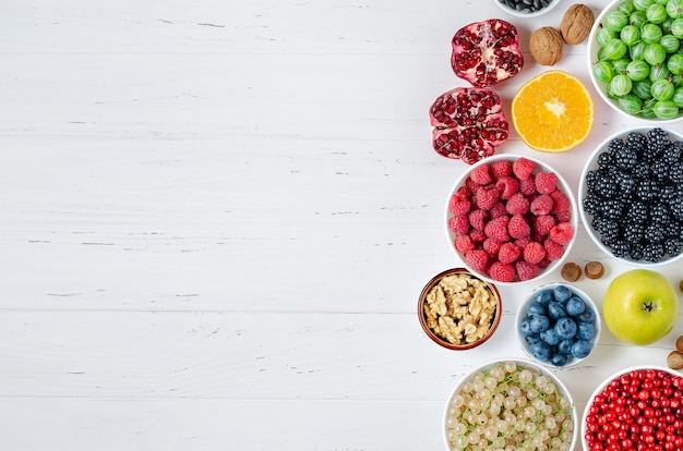 Fresh berries, fruits, nuts on a white wooden background. The concept of healthy eating. Food contains vitamins and trace elements. Copy space.