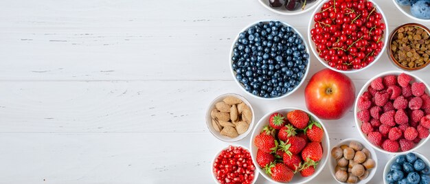 Fresh berries, fruits, nuts on a white wooden surface.