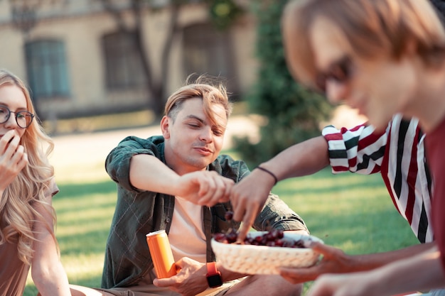 Fresh berries. Happy university friends eating cherries from the little basket enjoying summer during their picnic.