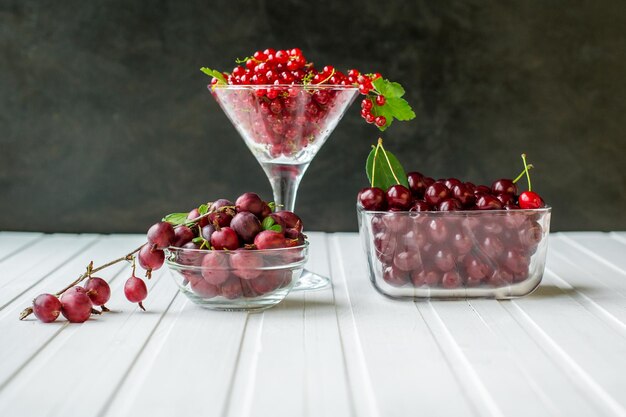 Свежие ягоды красной смородины и крыжовника в стеклянной посуде на кухонном деревянном столе