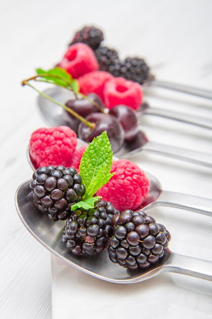 Fresh berries on steel spoons on white marble table