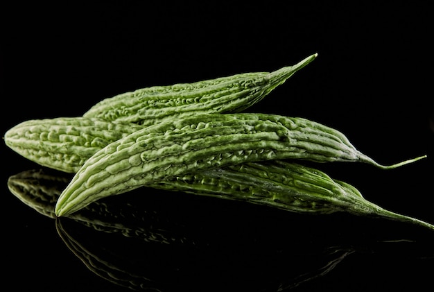 Fresh bitter melons isolated on black surface with reflection.