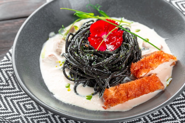 Fresh black tagliolini pasta with chicken in herbs on rucola and tomatoes