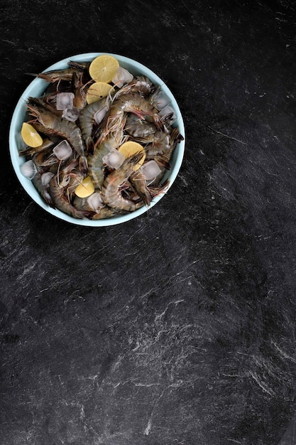 Fresh Black Tiger Shrimps on a Enamel Plate Ready for Preparation on a Rustic Black Marble Table,  with Lemon Garnish,  View from Above, Copy Space